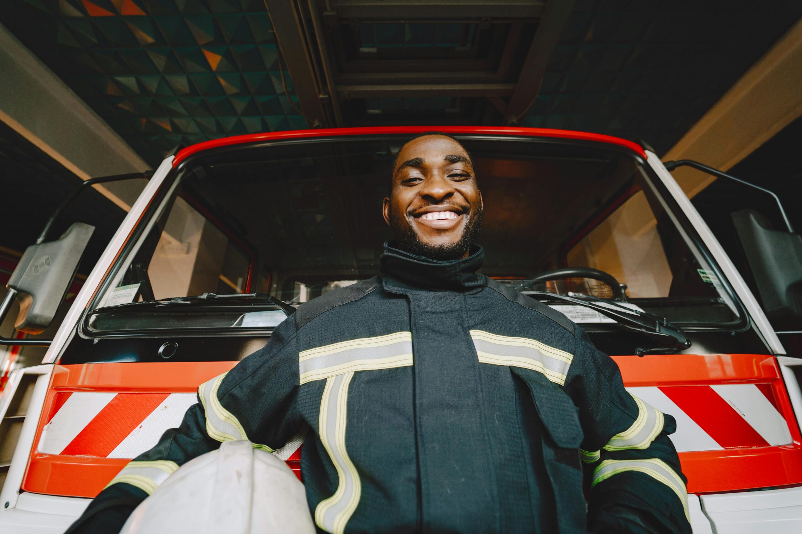 Smiling firefighter in safety gear standing in front of a fire truck, conveying bravery and readiness.